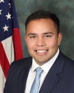 Person in a suit and tie standing in front of an American flag.